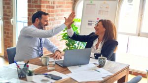 Two business professionals celebrating success with a high five during a workplace meeting on learning and development strategies